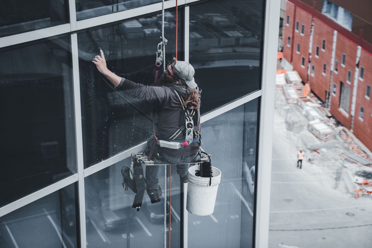 services-03 A worker cleaning skyscraper windows with a harness in an urban setting.